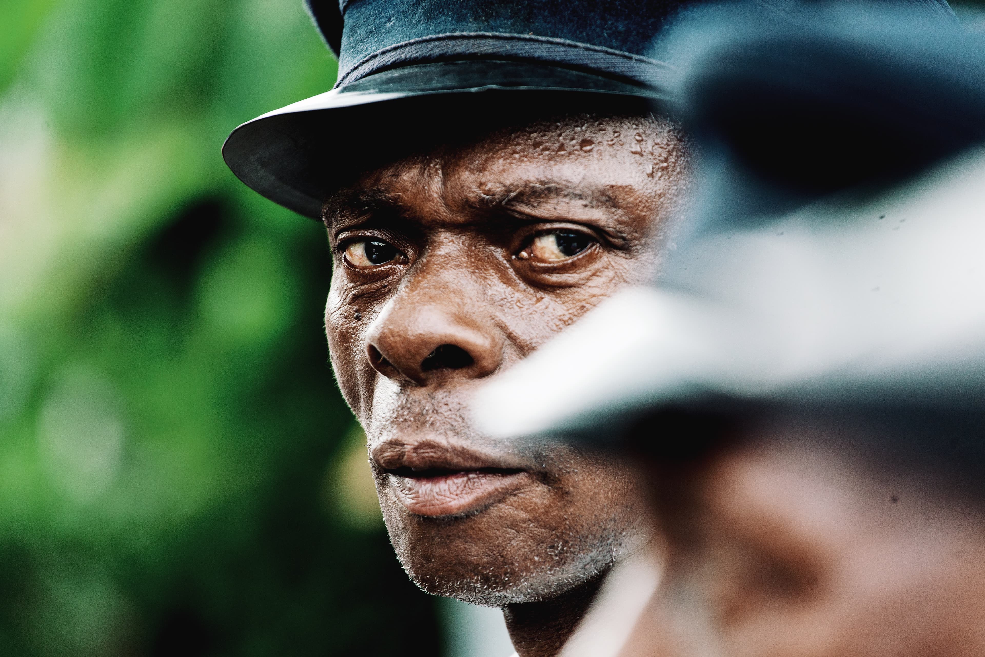 Um homem olha expressivamente para a câmera, com um chapéu preto na cabeça