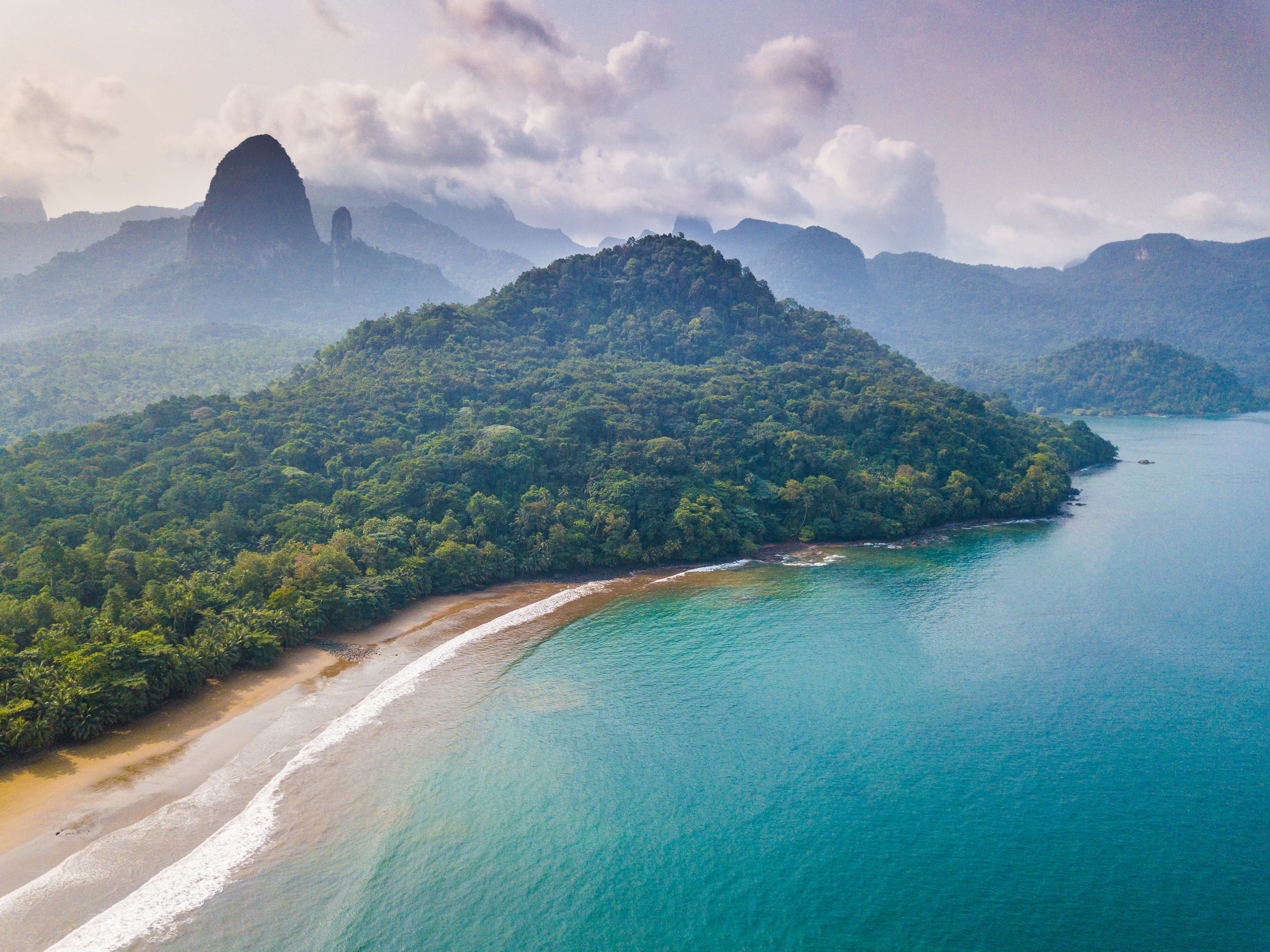 Vista da Ilha do Príncipe com água turquesa, praia, densa vegetação de selva e montanhas vulcânicas